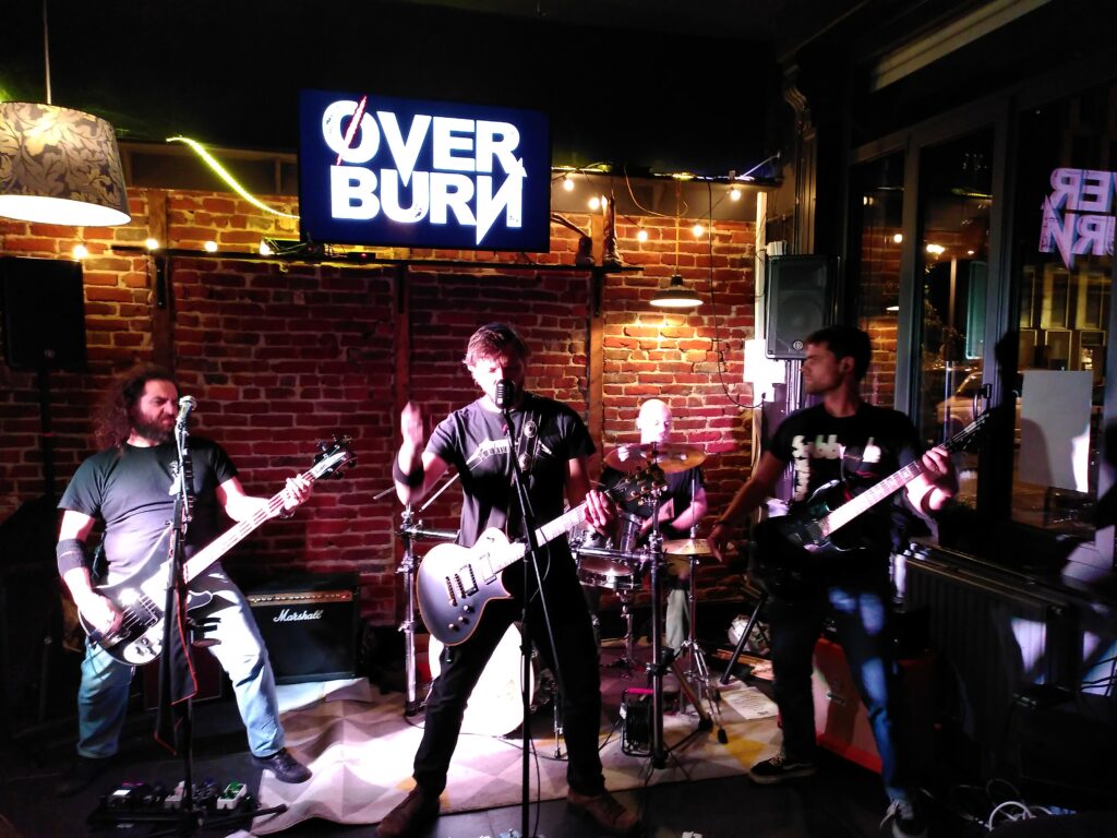 Photographie du groupe Øverburn en concert dans le bar Le Switch : bassiste, guitariste, batteur, guitariste